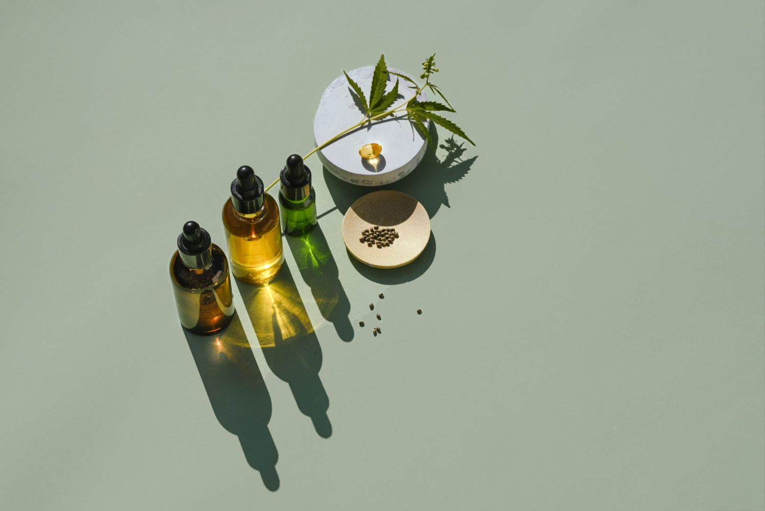 Various glass bottles with oil and tincture of CBD and a branch in hemp. Various cannabis products for food, sleep and personal care. Abstract trendy background for product presentation with cannabidiol, top view, minimal